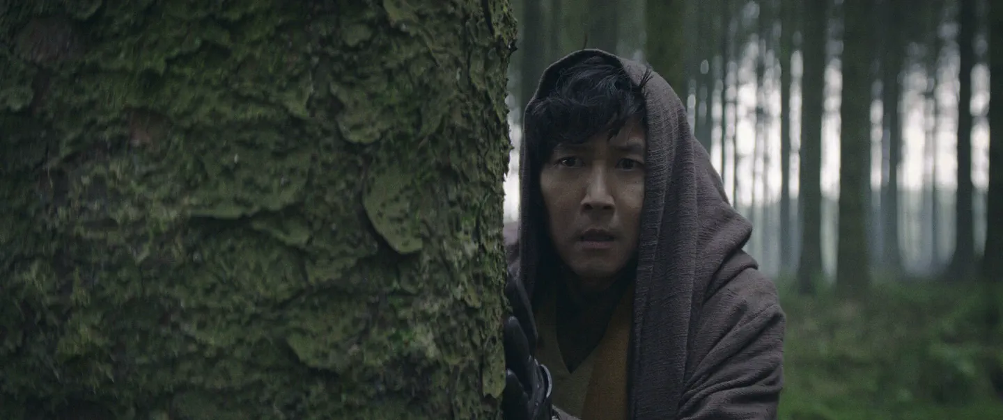 The Acolyte — a hooded figure takes cover behind a moss-covered tree in a mist-filled forest. Additional music by Orlando Pérez Rosso.