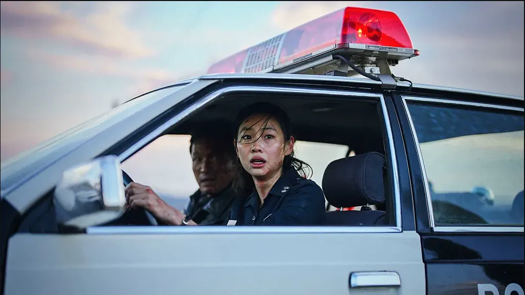 Hope — two mud-streaked survivors sit in a police car at dusk, its red lightbar burning above them. Additional music by Orlando Pérez Rosso.